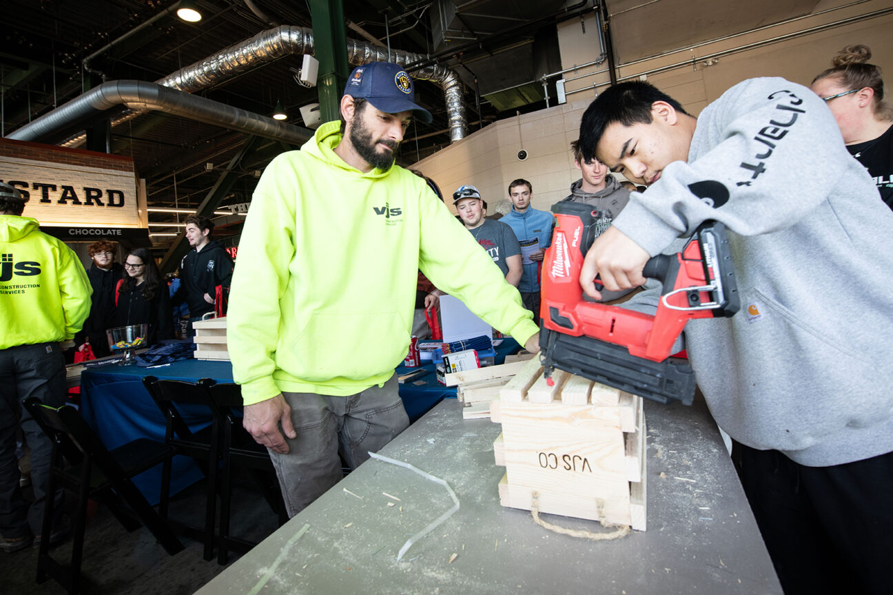 Zach Dorothy, a carpenter at VJS Construction Services (left) helps Greenfield High School senior Logan Plitt construct a wooden crate.